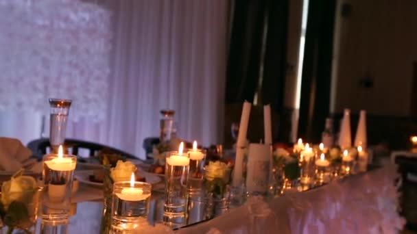 Detalhes do interior do salão do banquete de casamento com definição de mesa decorada no restaurante. Velas e pétalas brancas decoração com flores de rosas em vasos de vidro cheios de água . — Vídeo de Stock