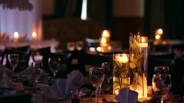 レストランに飾られたテーブルの設定で結婚式バンケット ホール内部詳細。ろうそくと水で満たされたガラスの花瓶のバラの花が付いている白い花弁装飾. — ストック動画