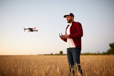 Quadcopter arka plan üzerinde uçan iken Çiftçi elleri ile uzaktan kumanda tutar. Buğday alanında bilimsel tarım uzmanı arkasında dron hovers. Tarım yeni teknolojiler ve yenilikler. Arkadan görünüm