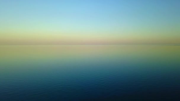 暖かい黄昏の海の表面の美しい穏やかな水に紫の夕日の空中映像。カメラは、カラフル パレット地平線のスカイラインと日の出の穏やかな海の上移動します。コンセプトをリラックスします。. — ストック動画