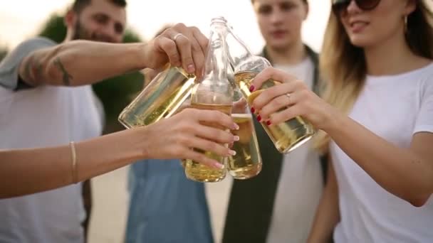 Groep vrienden plezier u geniet van een drankje en te ontspannen op het strand bij zonsondergang in slow motion. Jonge mannen en vrouwen drinken bier staande op een zand in de warme zomeravond. — Stockvideo