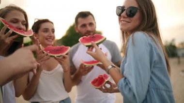 Mutlu arkadaş karpuz ayakta yemek Sandy Beach ve sohbet. Tatile denize yakın kot şort giyen kadın ve erkekler. Dostluk ve yaz konsepti