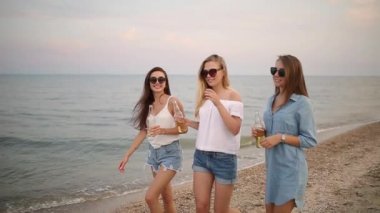 Grup kadın arkadaşıyla yavaş gün batımında sahilde denizin kenarında bir içecek zevk eğleniyor. Genç kadın bira veya kum üzerine sıcak yaz akşamları yürüyüş limonata içmek.