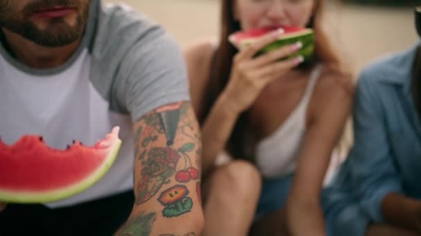 Happy Friends Eating Watermelon Sentado en Sandy Beach en vacaciones. Hombres y mujeres jóvenes que usan pantalones cortos vaqueros azules. Concepto de amistad y verano — Vídeos de Stock