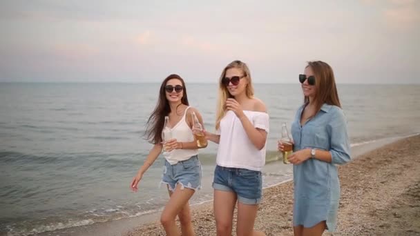 Group of female friends having fun enjoying a beverage on the beach by the sea at sunset in slow motion. Young women drink beer or lemonade walking on a sand in the warm summer evening. — Stock Video