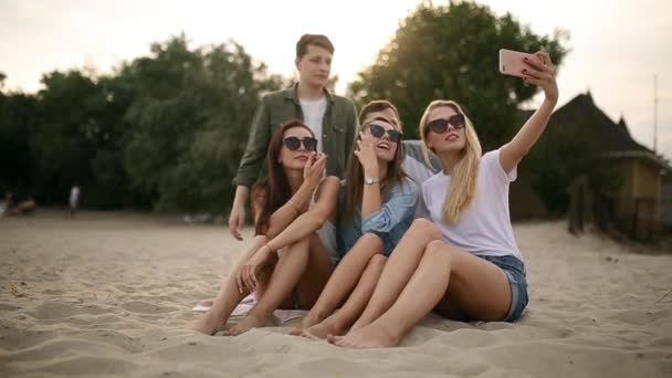 Fotografía de un grupo de jóvenes amigos tomando una selfie en la playa. Hombres y mujeres tomando fotos sentados en una arena en la cálida noche de verano . — Vídeos de Stock
