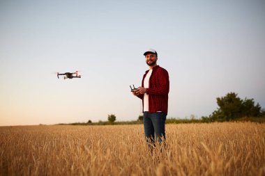 Quadcopter arka plan üzerinde uçan iken Çiftçi elleri ile uzaktan kumanda tutar. Buğday alanında bilimsel tarım uzmanı arkasında dron hovers. Tarım yeni teknolojiler ve yenilikler. Arkadan görünüm