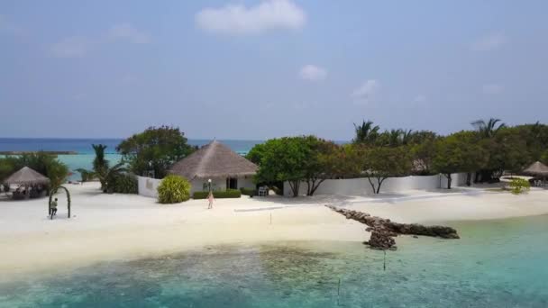 Vista aérea de mulher indo para bangalô spa no hotel resort ilha tropical com praia de areia branca, palmeiras e oceano Índico turquesa em Maldivas em 4k. Câmera Drone aproxima casa bungalow . — Vídeo de Stock