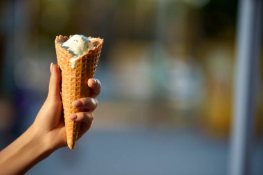 Dondurma külahı bulanık şehir bokeh arka plan ve boşaltmak kadın elinde. İzole görünümü Kapat, seçici odak. Erime ve buz çözme dondurma. Yaz tema.