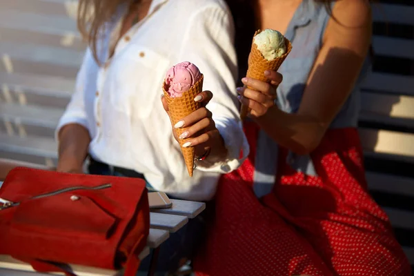 Vista isolada de duas amigas sentadas e segurando dois cones de sorvete em suas mãos no café ao ar livre. Jovens mulheres caucasianas casal oferecem sorvete no verão tempo quente em jaqueta de ganga . — Fotografia de Stock