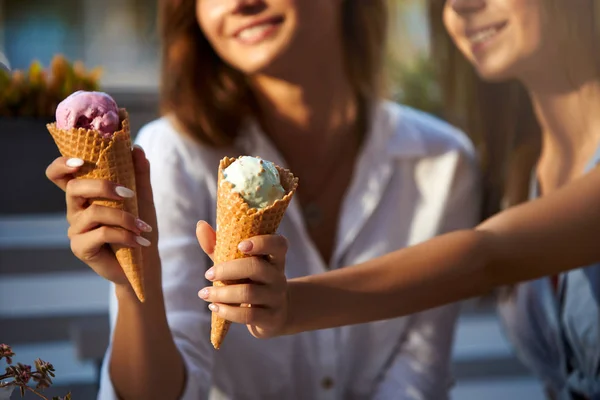 Close-up shot van ijs kegels in handen van een vrouw met haar vriend. Twee jonge vrouwen buitenshuis eten icecream op een zonnige dag. Geïsoleerd beeld, geen gezicht, copyspace voor ontwerpers. Thema zomer. — Stockfoto