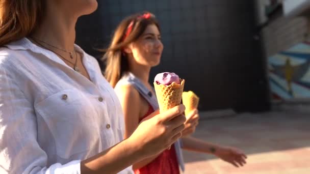 Крупный план рожков мороженого в руке женщины, идущей со своей подругой. Две молодые женщины на улице едят мороженое в солнечный день в городе. Изолированный вид, копирайс. Летняя тема . — стоковое видео