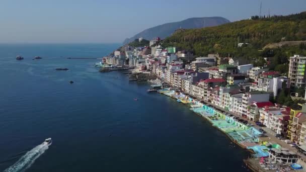 Antenowe drone footage kolorowy miasto miejski w górach, nad morze, Europa, gęste wielopiętrowego budynku nad morzem w ośrodku. Aparat wznosi się rosnącym do nieba. Prędkość łodzi przelotową w niebieski woda. — Wideo stockowe