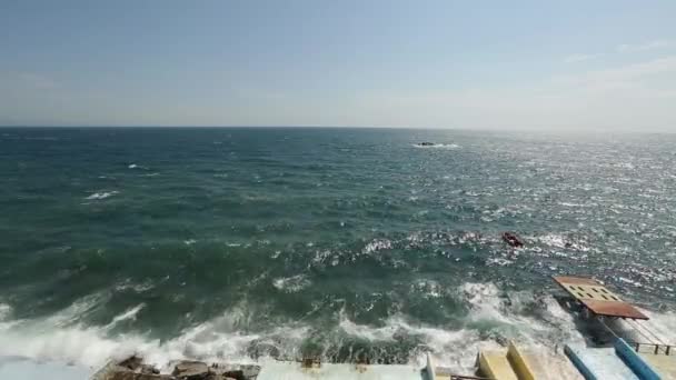 Enorme golven breken over waterkant van talud spatten en spuiten van druppels glazig zeewater omhoog in blauwe hemel. Storm in de zee op winderige dag. Opblaasboot rotsen op de golven. Kalmerende beelden. — Stockvideo