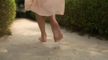 Arkadan görünüm kadının ayak exotical tropik adada spa Odalı Bungalov için gidiyor. Sarışın kız gülümseyerek yalınayak yakınındaki Maldivler avucunda beyaz kum yürür. Portrair görünüm