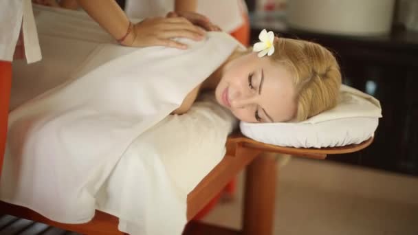 Primer plano de la hermosa mujer en la cama de spa en el complejo exótico. Linda chica rubia relajándose y teniendo un masaje con una flor en su pelo en Maldivas. Cámara en slider — Vídeos de Stock