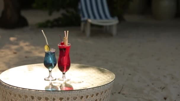 Dwa koktajle na stole na tropikalnej plaży. Napoje niebieski i różowy — Wideo stockowe