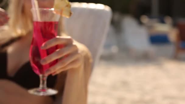 Mujer joven tomando el sol y bebiendo cóctel de colores en la playa tropical. Amante pasar la luna de miel tener vacaciones exóticas tumbado en el sol en la silla de cubierta cerca del océano — Vídeos de Stock