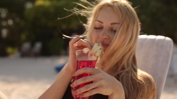 Güneşlenme ve içme genç kadın tropikal beach adlı kokteyl renkli. Harcama balayı egzotik tatil da Okyanusu yakınlarındaki şezlong üzerinde güneşte yalan olan sevgilisi — Stok video