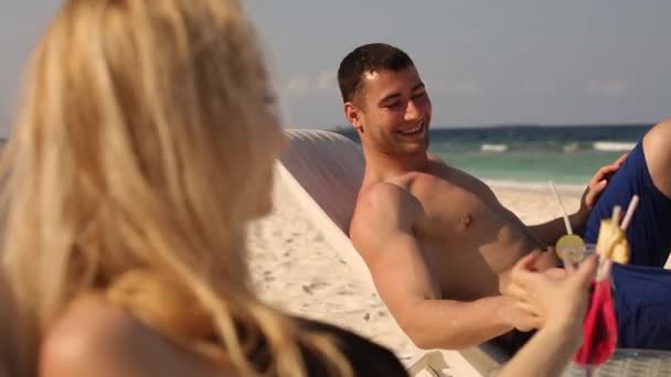 熱帯のビーチで日光浴や飲む家族カップル色カクテル。新婚旅行愛好家は、海の近くのデッキチェアの上で横になっているエキゾチックな休暇を持っています。 — ストック動画