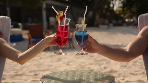 Junges Familienpaar sonnt sich und trinkt einen farbigen Cocktail am tropischen Strand. Liebhaber auf Flitterwochen haben exotischen Urlaub in der Sonne liegend auf Liegestühlen am Meer — Stockvideo