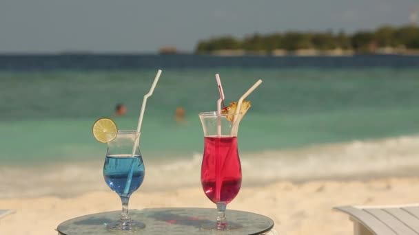 热带海滩桌上有两杯鸡尾酒。蓝色和粉红色饮料 — 图库视频影像