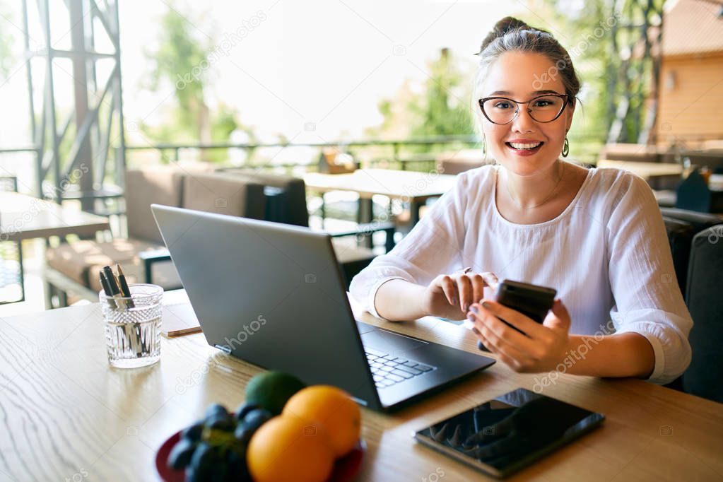 Young mixed race woman working with laptop in cafe looking at camera. Asian caucasian female studying using internet. Business woman doing social marketing work and shopping. Telecommuting concept.