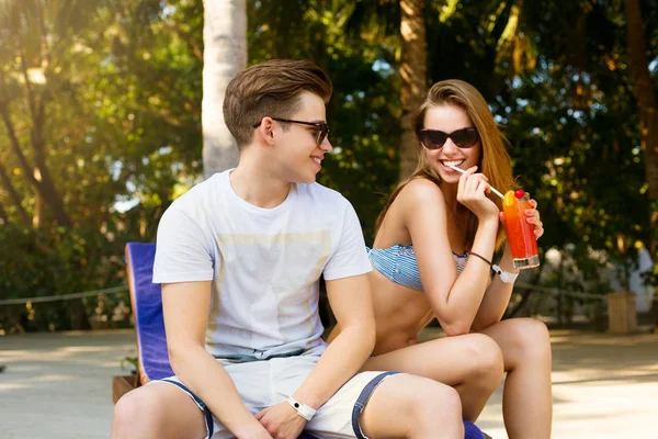 Passar tempo despreocupado junto à piscina. Casal feliz segurando coquetéis e sorrindo enquanto se senta nas cadeiras ao lado da piscina. Conceito de férias — Fotografia de Stock