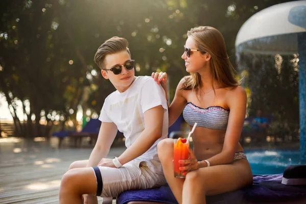 Passar tempo despreocupado junto à piscina. Casal feliz segurando coquetéis e sorrindo enquanto se senta nas cadeiras ao lado da piscina. Conceito de férias — Fotografia de Stock