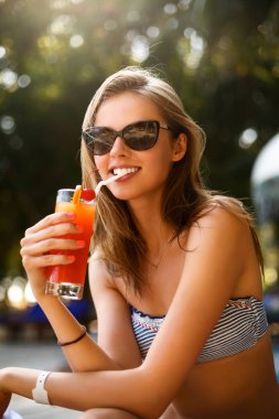 Kokteyl cam tropik güneşin Yüzme Havuzu palmiye ağaçları ile güverte sandalyeye yakınındaki tüyler ürpertici olan kadın portresi. Tatil kavramı