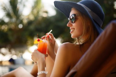 Kokteyl cam tropik güneşin Yüzme Havuzu palmiye ağaçları ile güverte sandalyeye yakınındaki tüyler ürpertici olan kadın portresi. Tatil kavramı