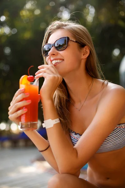背後にヤシの木とサンラウン ジャーにプールの近くの熱帯の太陽で冷やしてカクテル グラスを持つ若い女性の肖像画。休暇の概念 — ストック写真