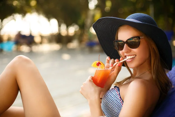 Portrait of young woman with cocktail glass chilling in the tropical sun near swimming pool on a deck chair with palm trees behind. Vacation concept — Stock Photo, Image
