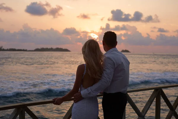 Visão traseira de recém-casados abraçar uns aos outros e ver o horizonte do pôr do sol na praia tropical ilha em Maldivas. Lagoa azul-turquesa no fundo. Conceito de lua de mel . — Fotografia de Stock