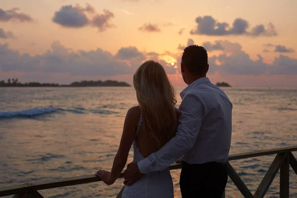 Visão traseira de recém-casados abraçar uns aos outros e ver o horizonte do pôr do sol na praia tropical ilha em Maldivas. Lagoa azul-turquesa no fundo. Conceito de lua de mel . — Fotografia de Stock