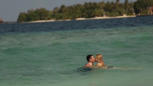 可爱的情侣在一个空旷的海滩上在印度洋游泳。两个恋人在蓝色翡翠海蜜月沐浴亲吻的画面 — 图库视频影像