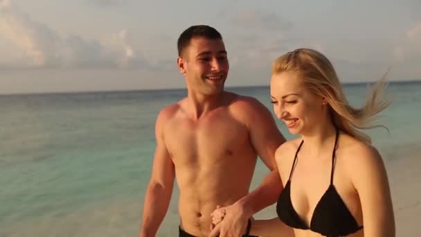 Молодая пара бегает по пляжу в сёрфе, держась за руки. Молодожёны в медовом месяце наслаждаются отпуском. Любовники брызгают голубой морской водой после свадьбы . — стоковое видео