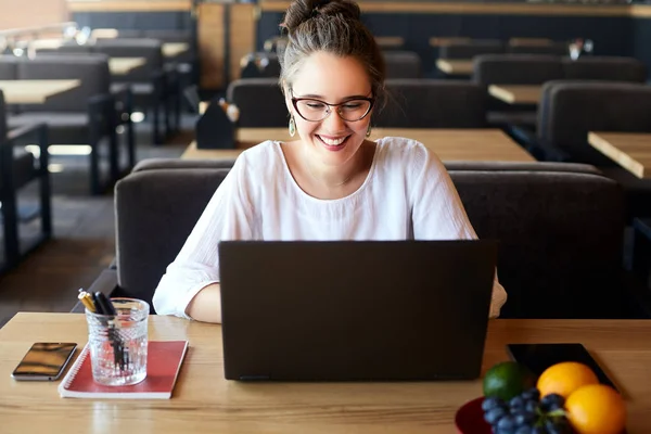 Mujer joven de raza mixta que trabaja con el ordenador portátil en la cafetería. Asiática mujer caucásica estudiando usando internet. Mujer de negocios haciendo trabajo de marketing social y compras. Concepto de teletrabajo . — Foto de Stock