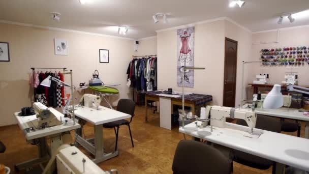 Empty designer atelier interior with tables and sewing machines. Equipped fashion tailoring studio indoors with clothes and reels of threads, no people. — Stock Video