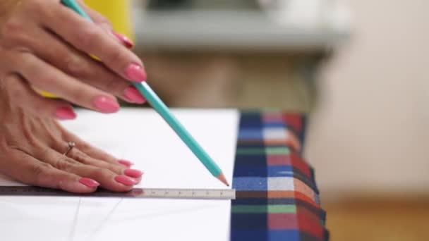 Stäng Visa modedesigner kvinna händer arbetar i studio. Kaukasiska kvinnliga skräddare ritning layout för kläder på tyg med hjälp av penna och linjal. Atelier inomhus. — Stockvideo