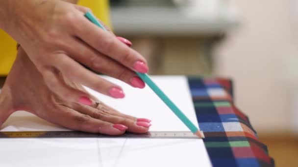 Тесный вид на женские руки модельера, работающего в студии. Кавказская портная рисует макет одежды на ткани карандашом и линейкой. Atelier в помещении . — стоковое видео