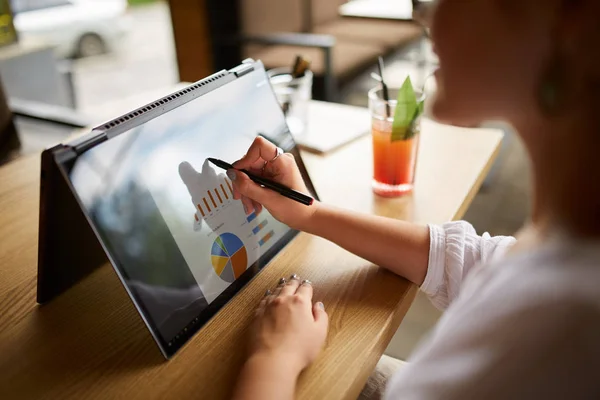 Businesswoman hand pointing with stylus on the chart over convertible laptop screen in tent mode. Woman using 2 in 1 notebook with touchscreen for work on business presentation. Isolated close view.