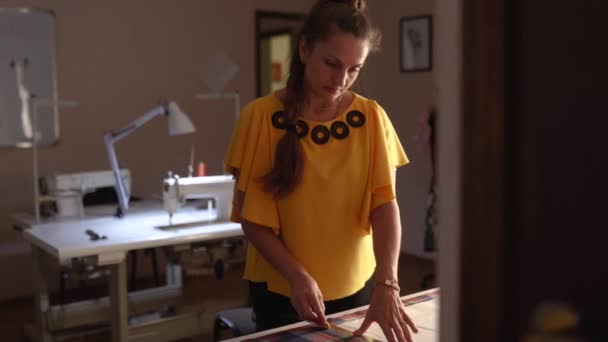 Mujer diseñadora de moda trabajando en el estudio. Sastre femenino caucásico dibujando el diseño para la ropa en tela usando tiza y regla. Atelier en interiores . — Vídeos de Stock