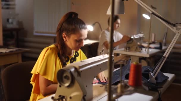 Dressmaker trabalhando em uma máquina de costura no estúdio sob medida à mesa. Ocupação profissional de costureira em oficina de moda. Estudante trabalhando no fundo no atelier dentro de casa . — Vídeo de Stock