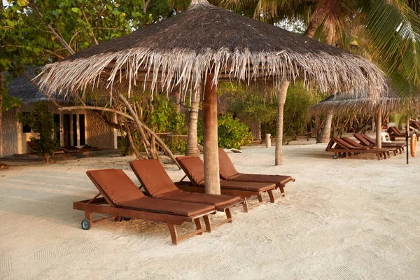 Beach deck chairs under straw umbrellas. Indian ocean coastline on Maldives island. White sandy beach and calm sea. Travel and vacation concept. — Stock Photo, Image