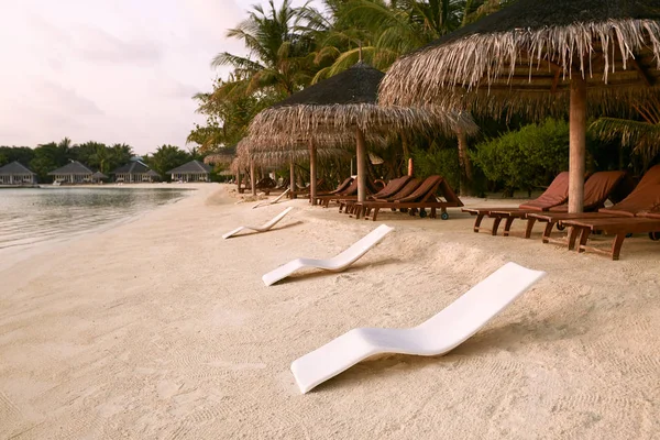 Strandstoelen onder stro paraplu's. De kustlijn van de Indische Oceaan op Maldiven island. Wit zandstrand en kalme zee. Reizen en vakantie concept. — Stockfoto