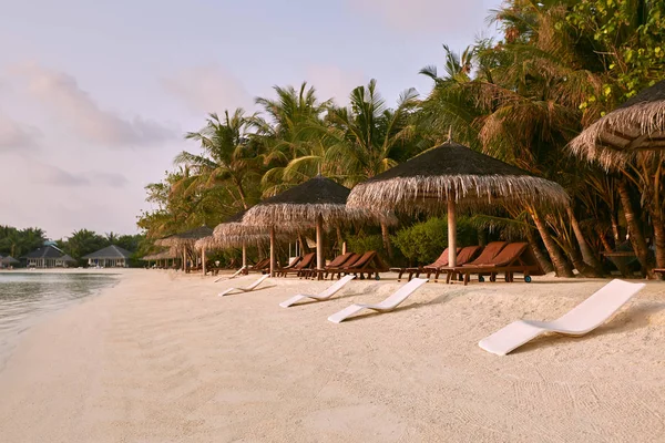 Beach chairs under straw umbrellas. Indian ocean coastline on Maldives island. White sandy beach and calm sea. Travel and vacation concept. — Stock Photo, Image