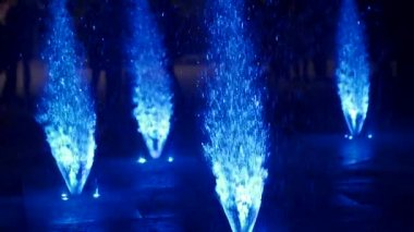 Geceleri renkli dans eden çeşme. Su jetleri karanlık bir arka plan üzerinde ağır çekim portre görüntüleri. Tanınmayan insanlar siluetleri.