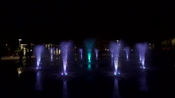 カラフルな噴水ショー夜。暗い背景に水のジェット機のスローモーション映像。認識できない人々 のシルエット. — ストック動画