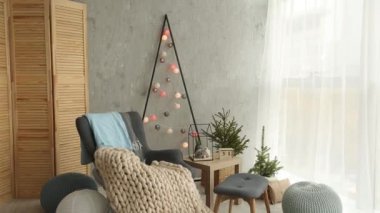 Bir şık koltuk ve sıcak merinos ekose ile şık Noel İskandinav iç. Konfor nordic Yılbaşı dekor ile ev. Çelenk ve ışık oda ışıkları ile minimalist Noel ağacı.